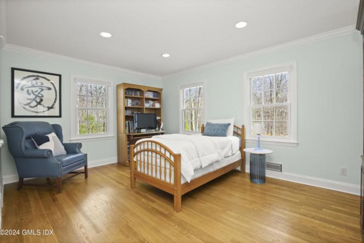 A bedroom with a bed, shelf, studio couch, painting, and windows.