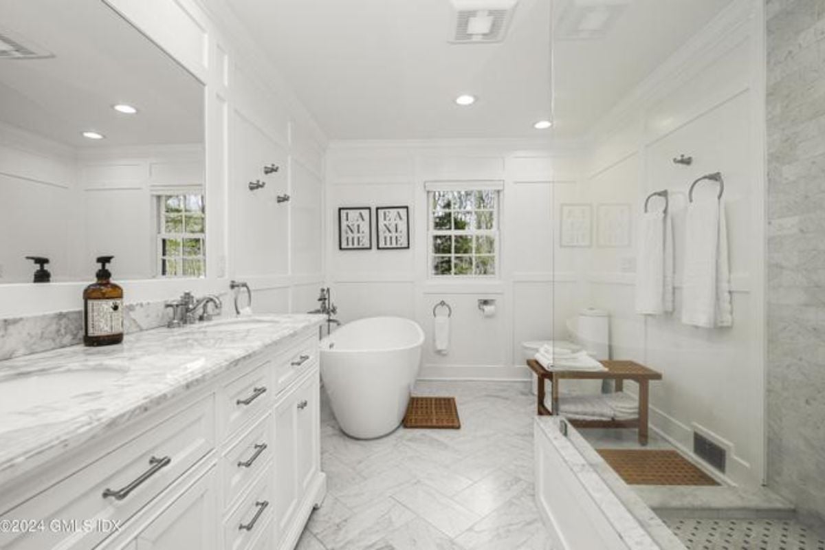 A bathroom with a tiled floor, dual vanity, mirror, and bathtub.