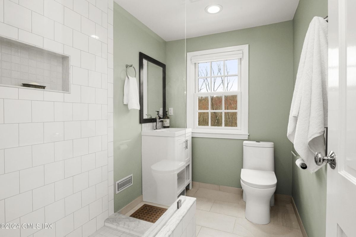 A bathroom with a vanity, mirror, window, and toilet.