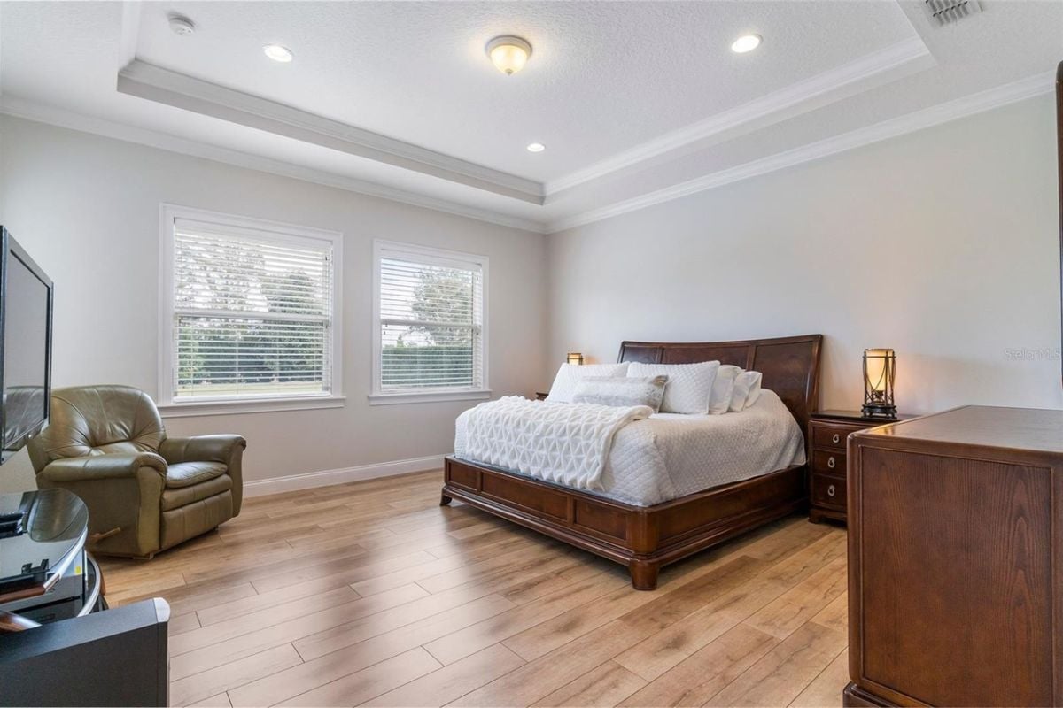 A bedroom with a bed, windows, a studio couch, nightstand, cabinet, and TV.