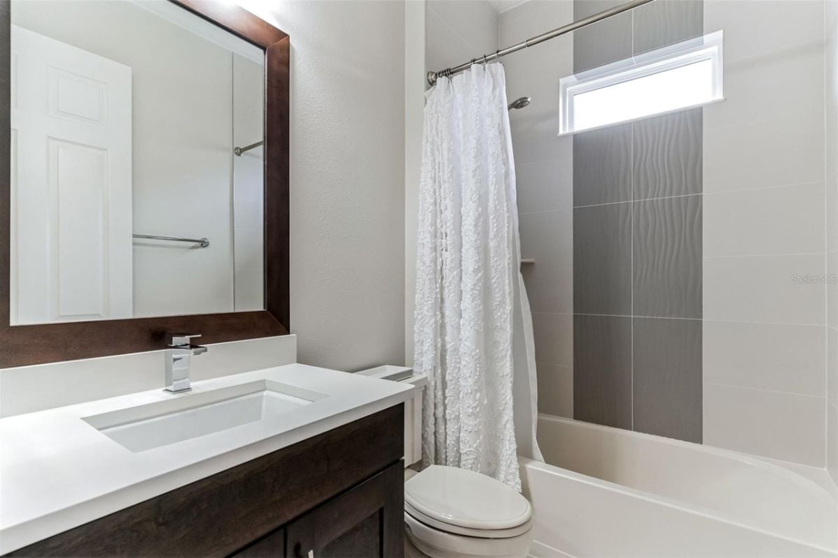 A bathroom with a vanity, mirror, toilet, and bathtub.