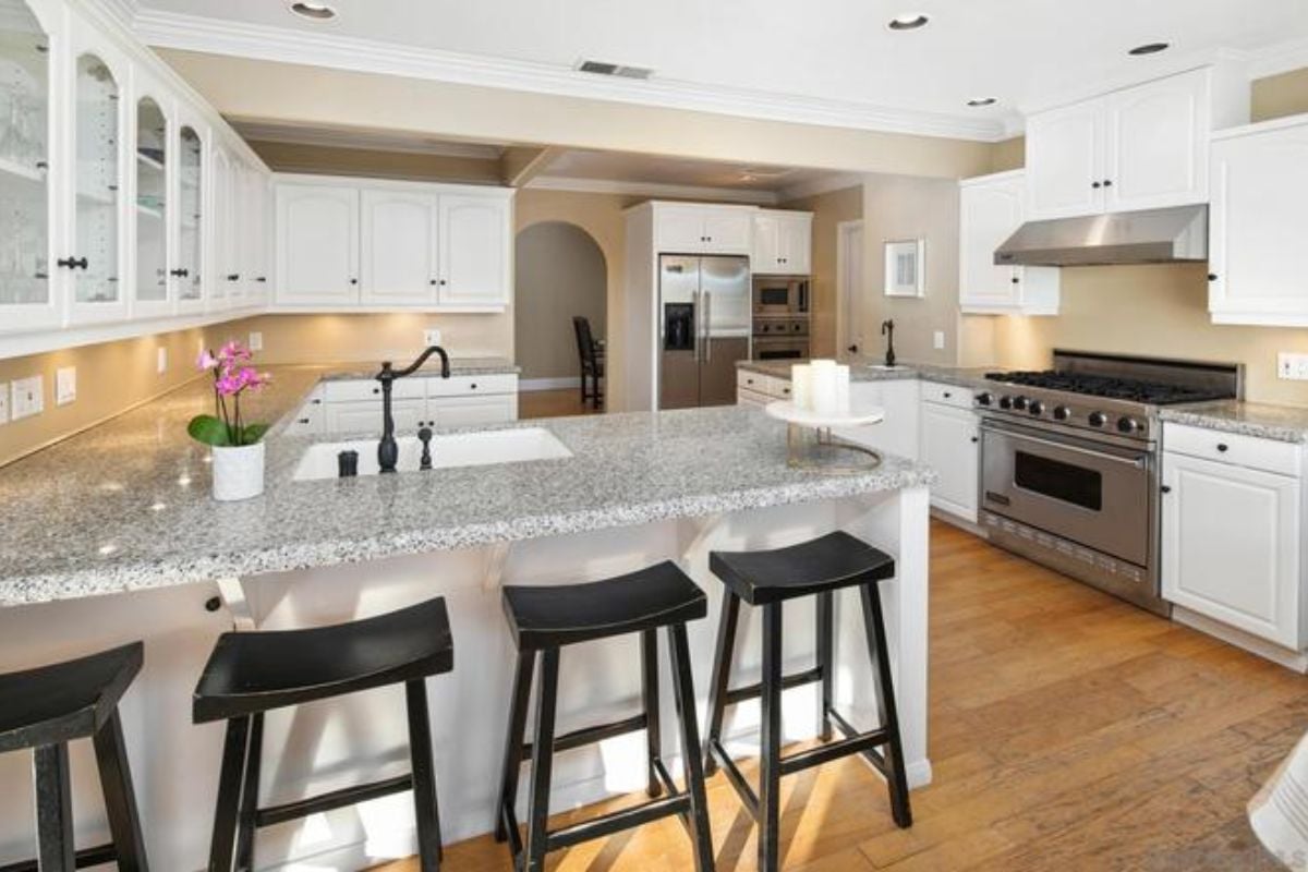 A kitchen with countertops, stools, sink, cabinets, and a stove.