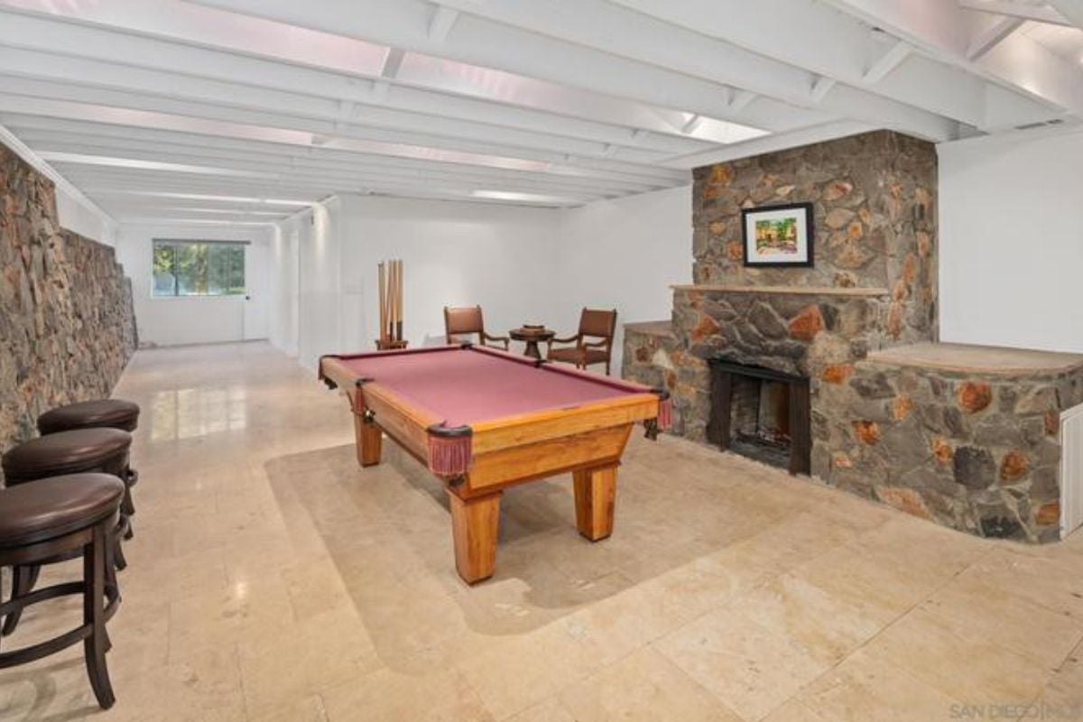 A game room with stone walls, a stone fireplace, an exposed beam ceiling, a tiled floor, and a pool table.