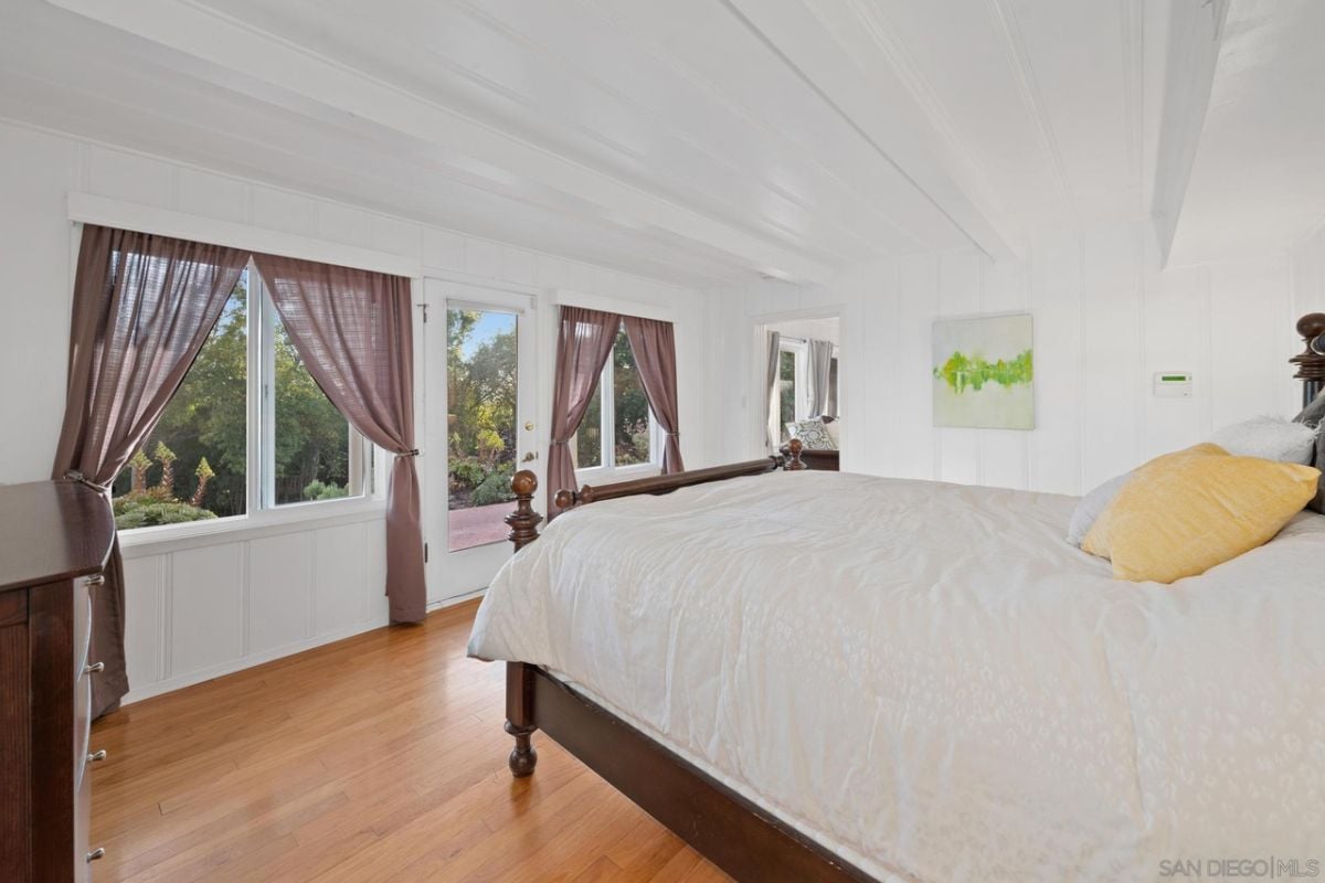 A bedroom with a bed, windows with curtains, and a cabinet.