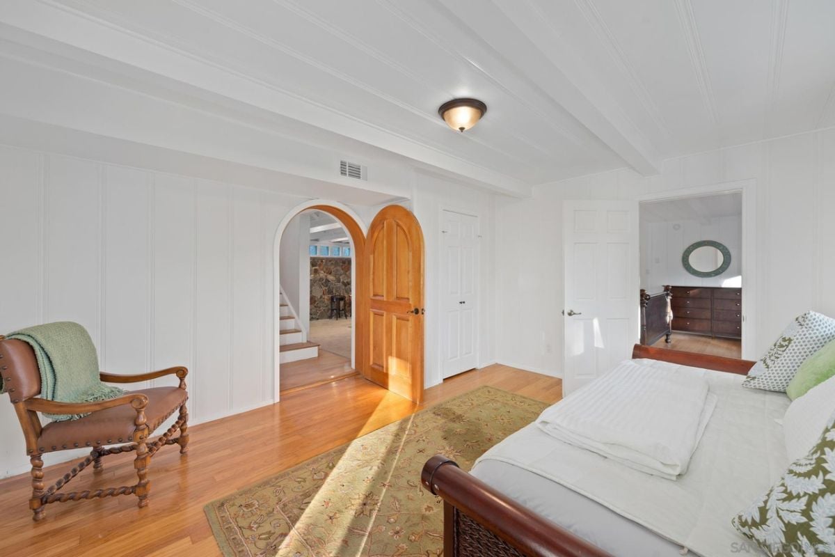 A bedroom with a bed, rug, mirror, and chair.