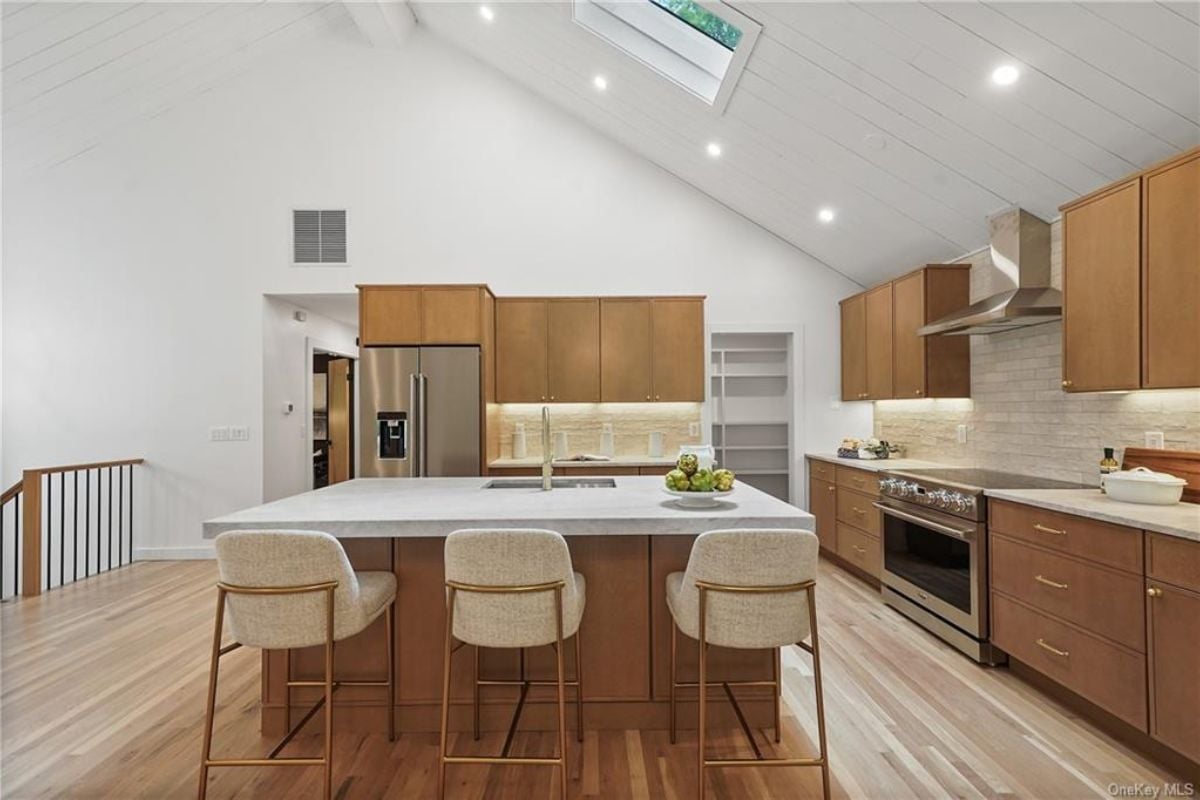 A kitchen with an island, stools, countertop, cabinets, and a stove.