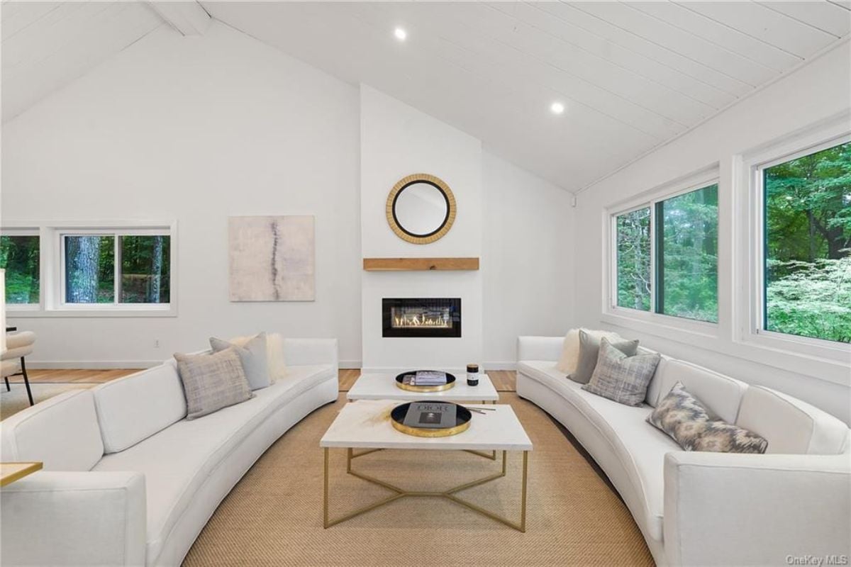A living room with a fireplace, window, white couches, and a center table.