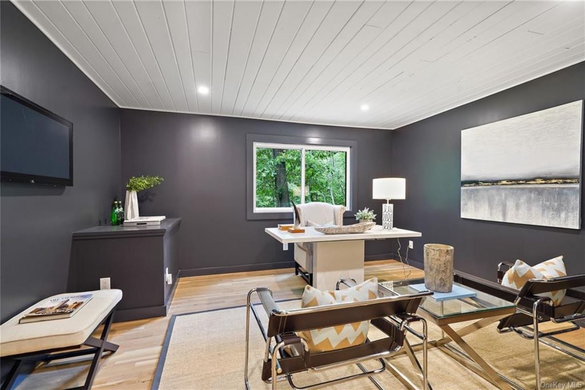 A home office with a painting, window, cabinet, TV, desk, and chairs.
