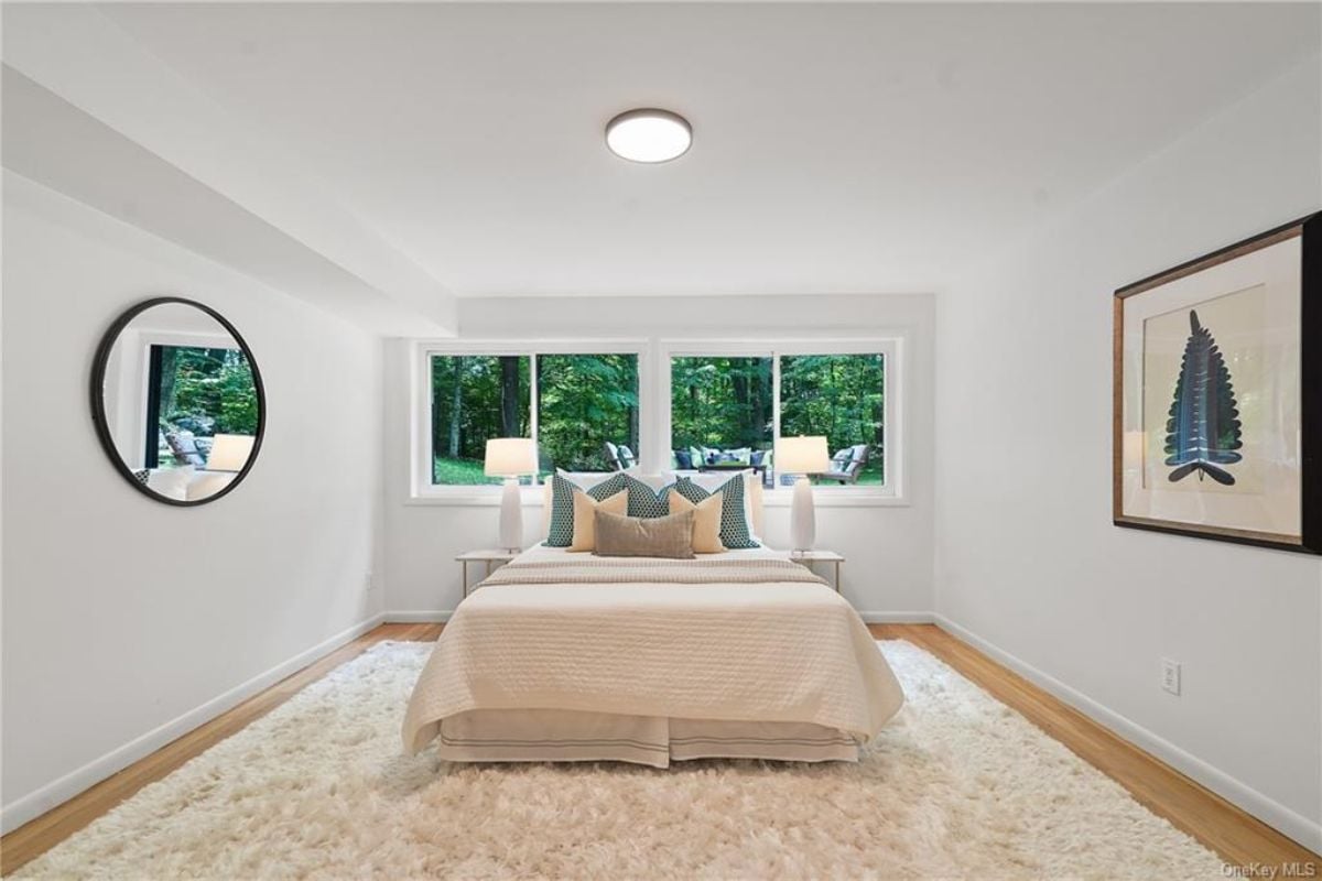 A bedroom with a bed, windows, a mirror, and a painting.