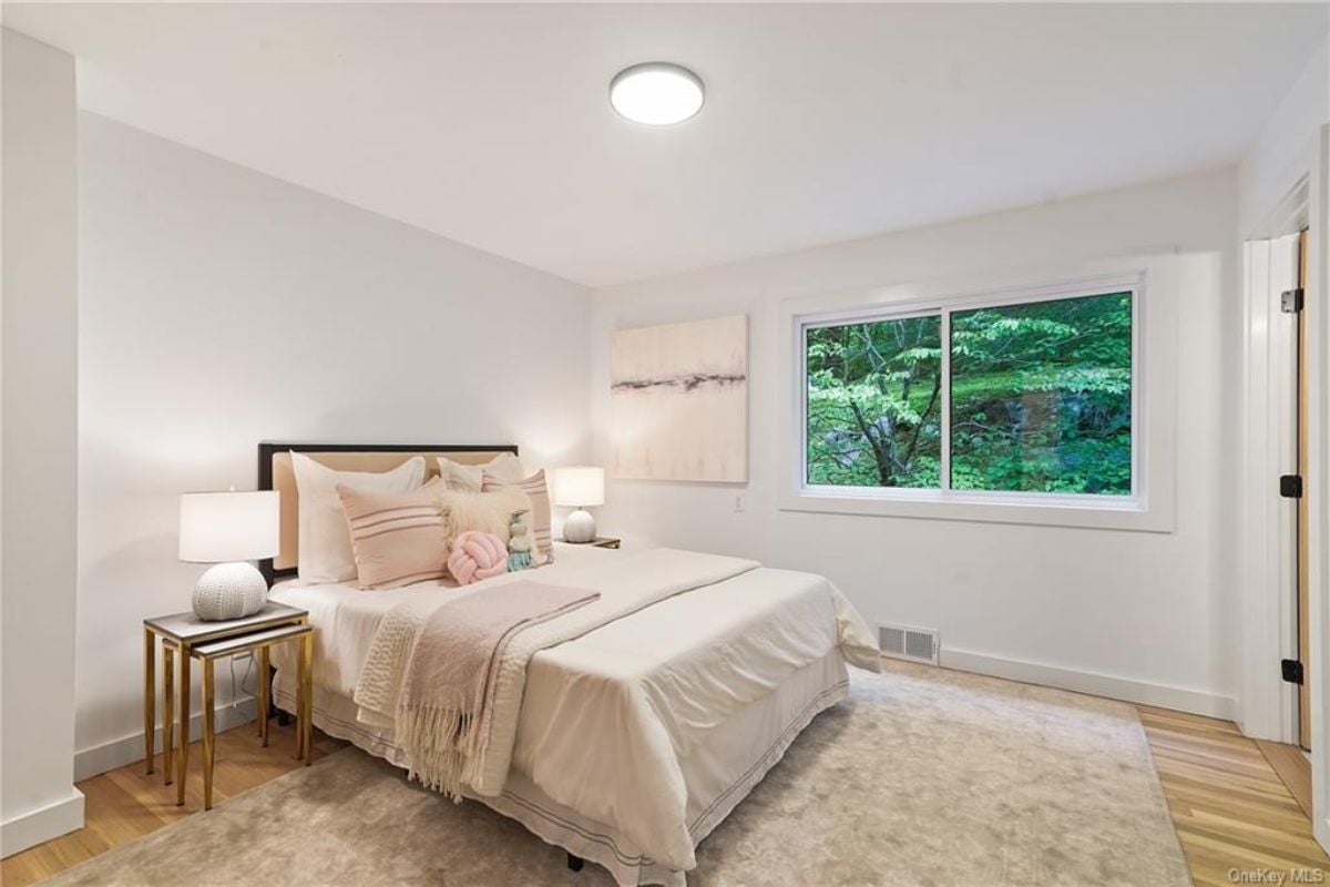 A bedroom with a bed, windows, a nightstand, and a painting.