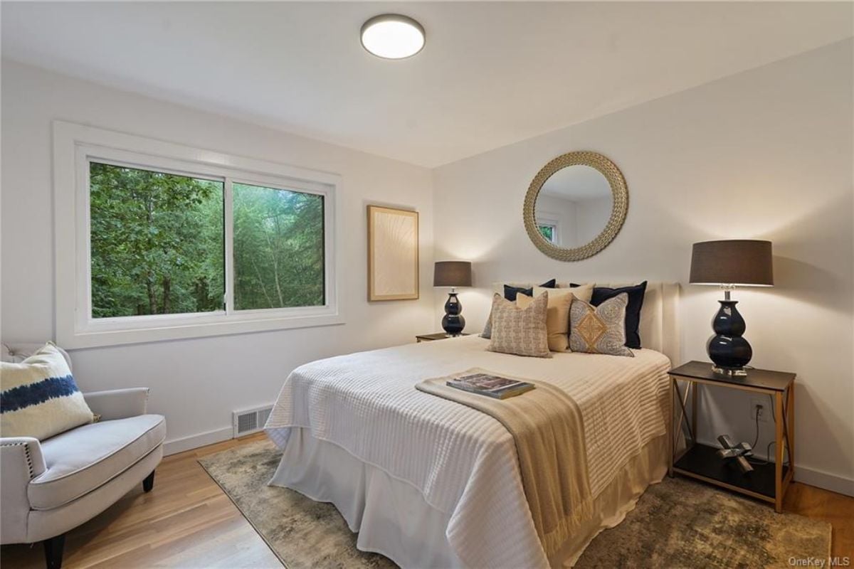 A bedroom with a bed, windows, a mirror, a nightstand, a studio couch, and a painting.