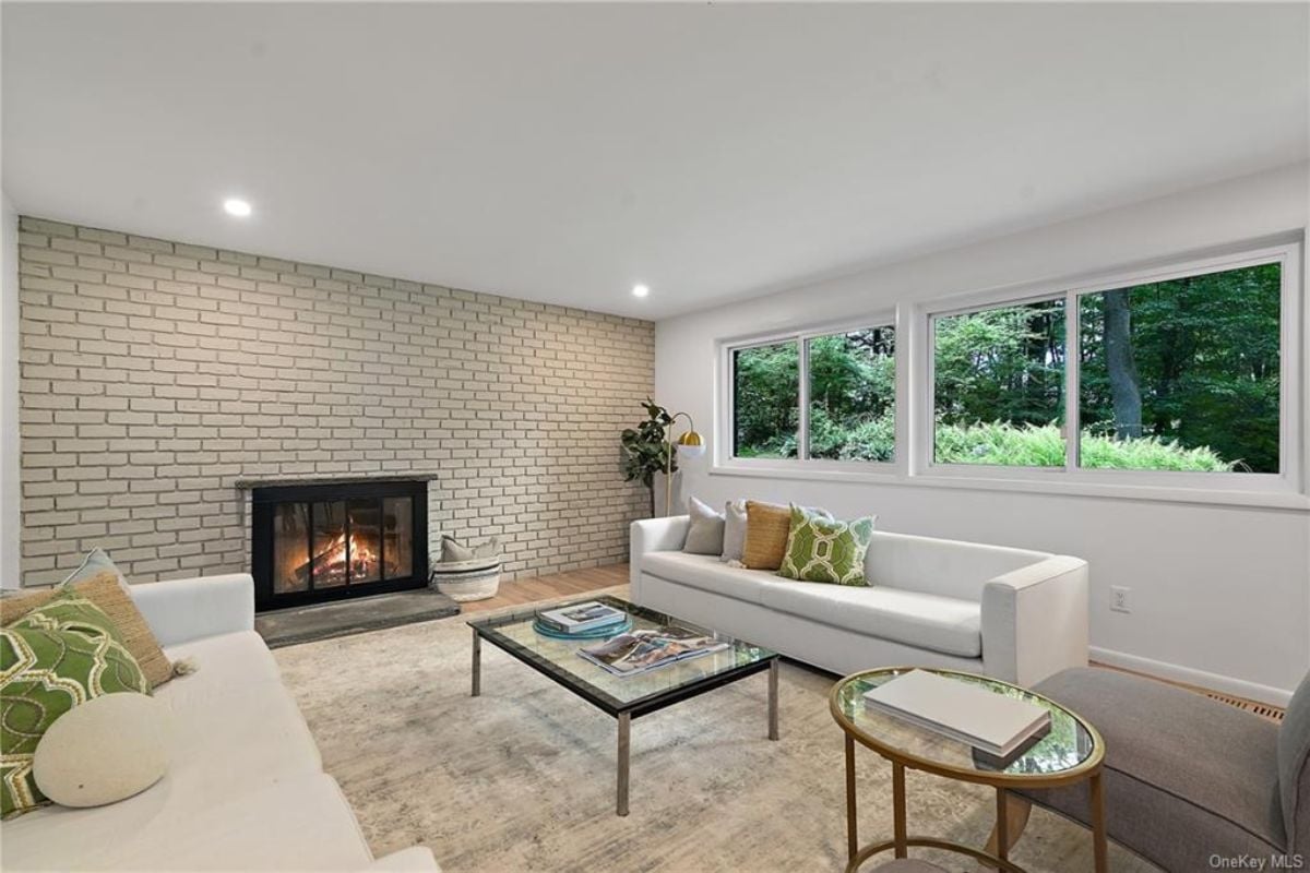 A living room with a brick fireplace, windows, white couches, and a center table.