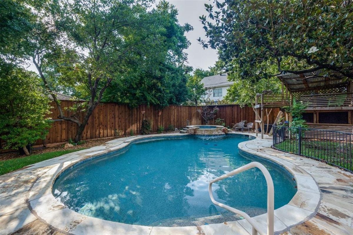 A swimming pool with a jacuzzi, surrounded by plants and trees.