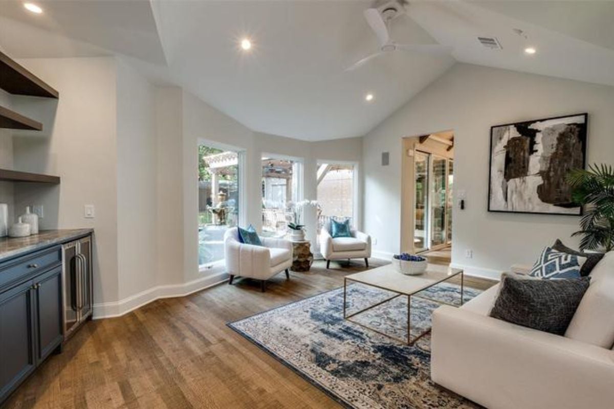 A lounge with chairs, a couch, a painting, a ceiling fan, and a coffee table.