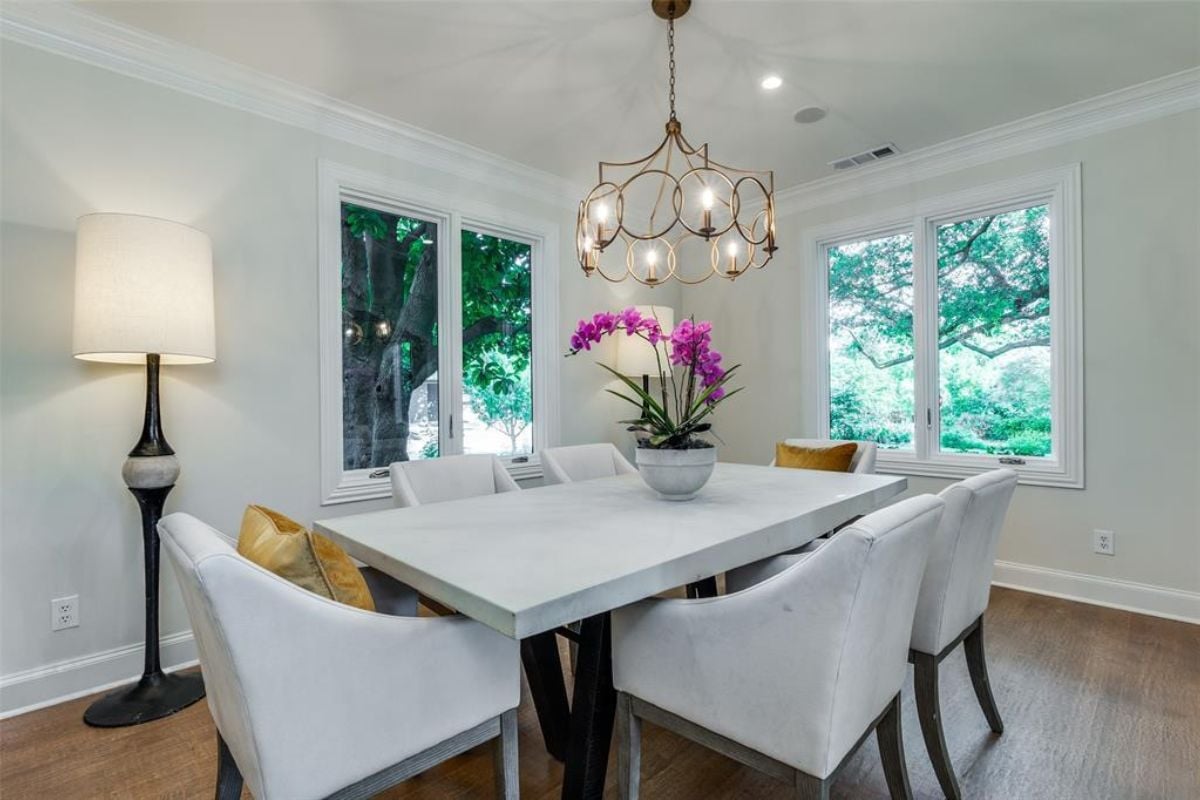 A dining room with windows, a chandelier, and a dining table surrounded by chairs.