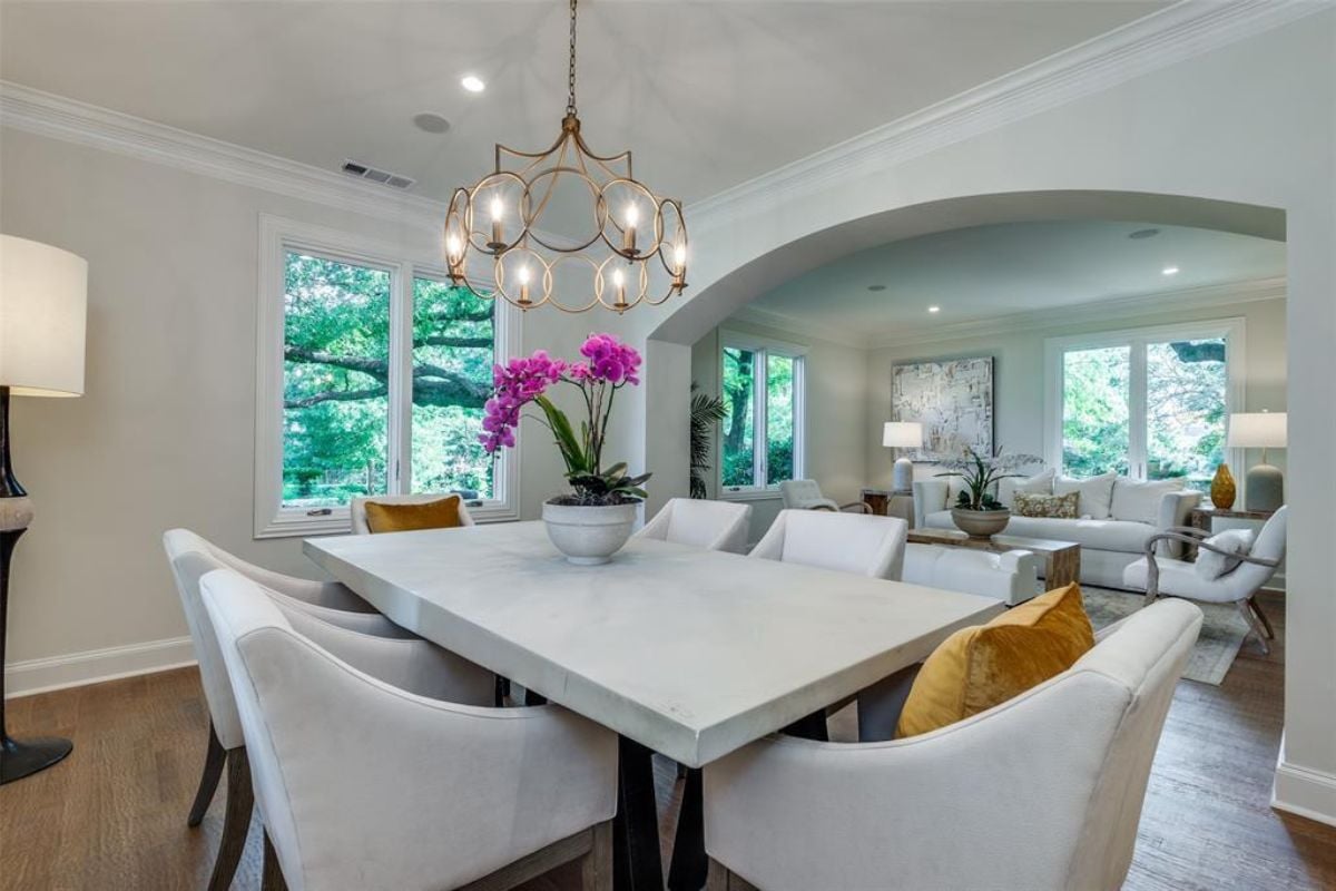 A dining room with windows, a chandelier, and a dining table surrounded by chairs.