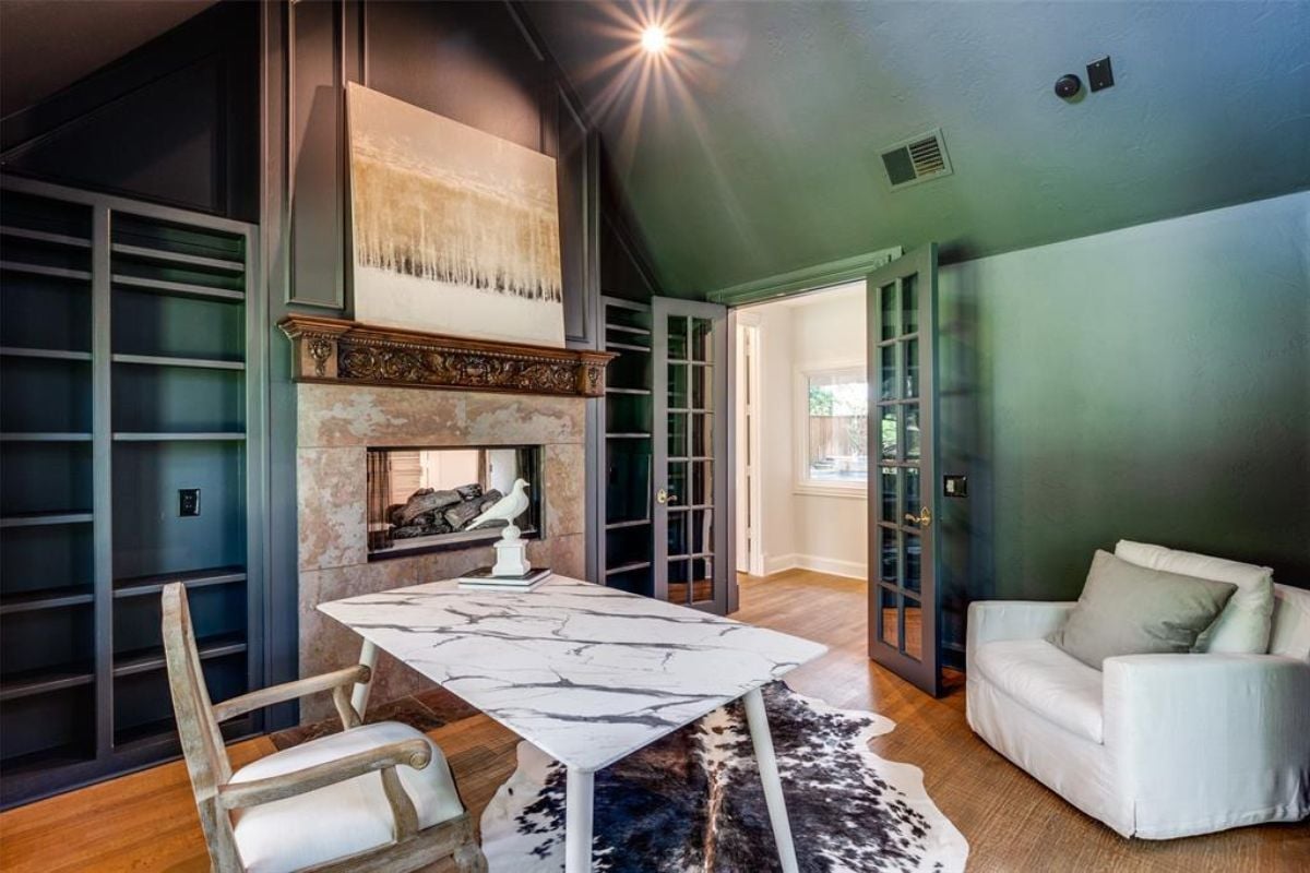 A home office with a fireplace, painting, chair, desk, and studio couch.