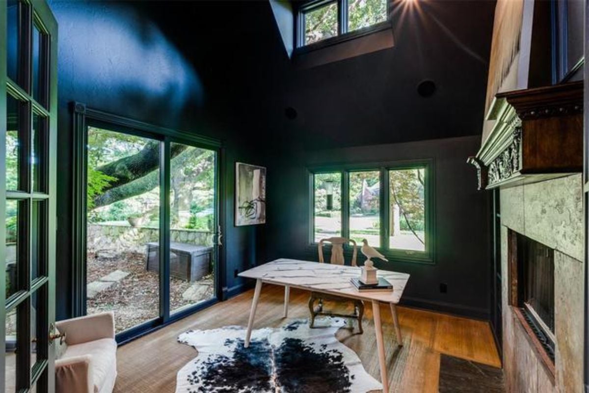 A home office with a fireplace, painting, chair, desk, and studio couch.
