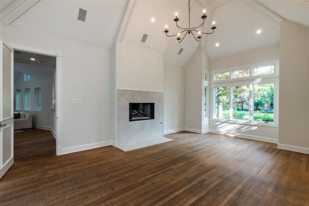 An empty room with a vaulted ceiling, chandelier, fireplace, and wooden floor.