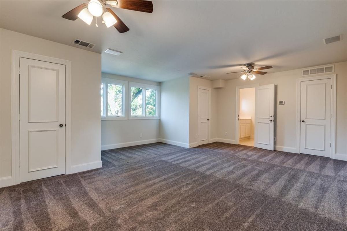 An empty room with a white ceiling, windows, and ceiling fans on the floor.