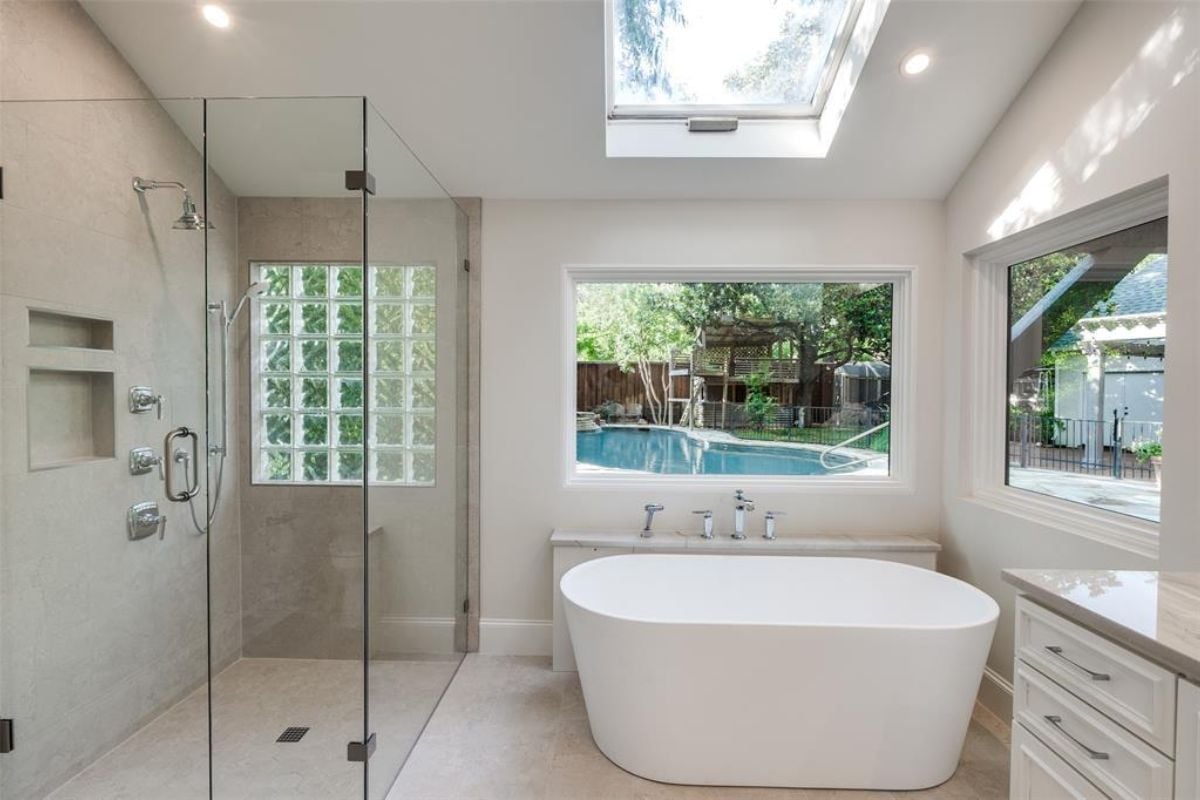 A bathroom with windows, a skylight roof, a bathtub, and a glass shower room.