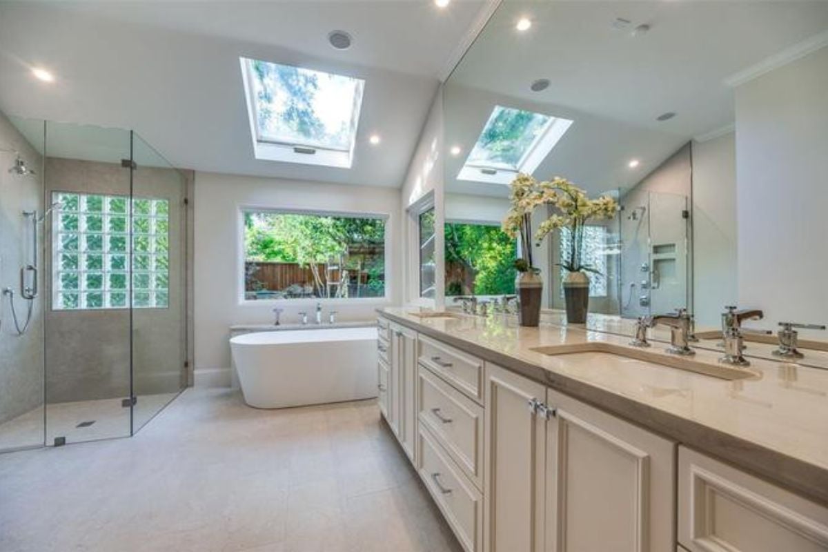 A bathroom with countertops, sink, mirror, cabinets, a bathtub, glass shower room, and skylight roofing.