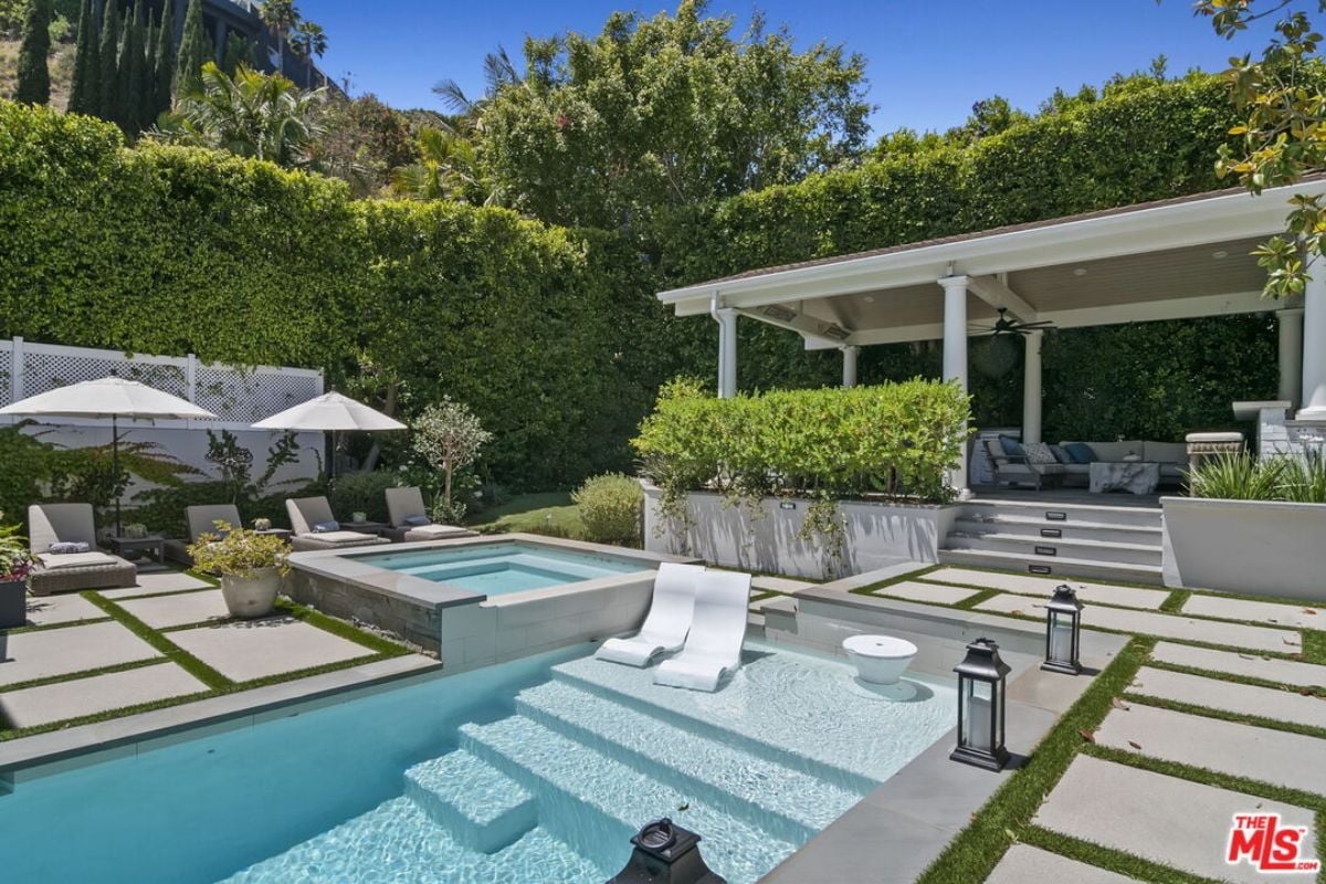 A swimming pool with a Jacuzzi, surrounded by plants and trees.