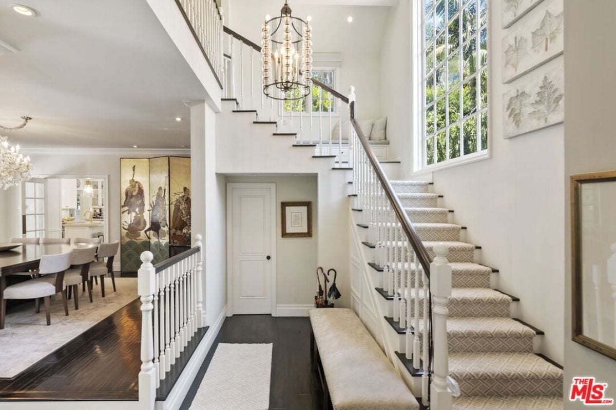 A foyer with a chandelier, bench, and staircase.