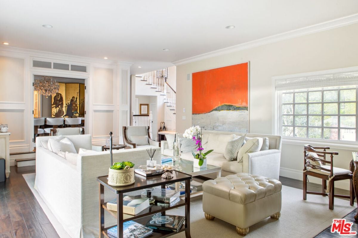 A living room with paintings, chairs, white couches, and a center table.
