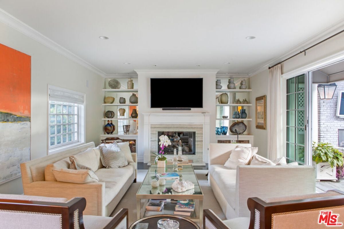 A living room with shelves, a TV, windows, a fireplace, couches, and a center table.