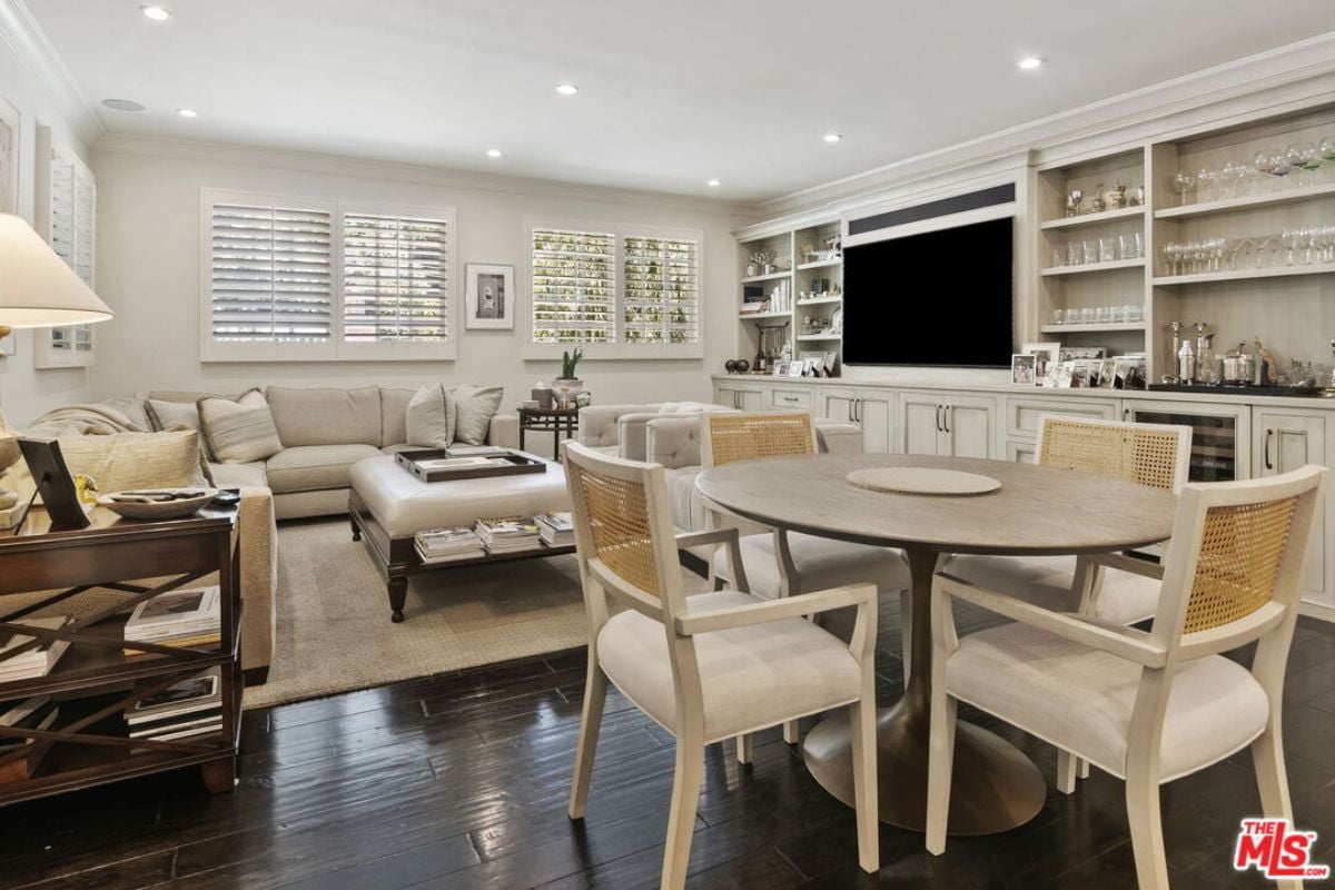 A family room with shelves, a TV, windows, cabinets, couches, and a round table surrounded by chairs.