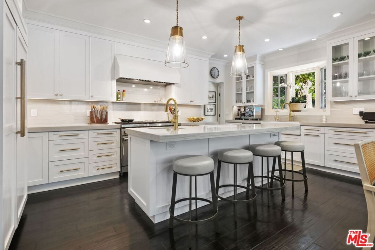 A kitchen with countertops, stools, sink, cabinets, and kitchen appliances.