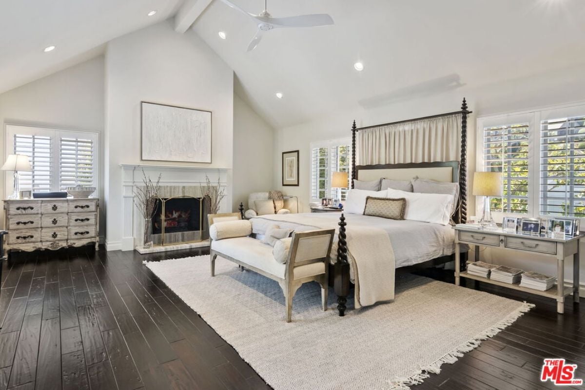 A bedroom with a bed, vaulted ceiling, ceiling fan, windows, fireplace, cabinets, and a nightstand.