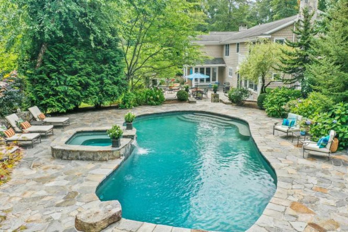 A swimming pool with chairs on the poolside surrounded by plants and trees.