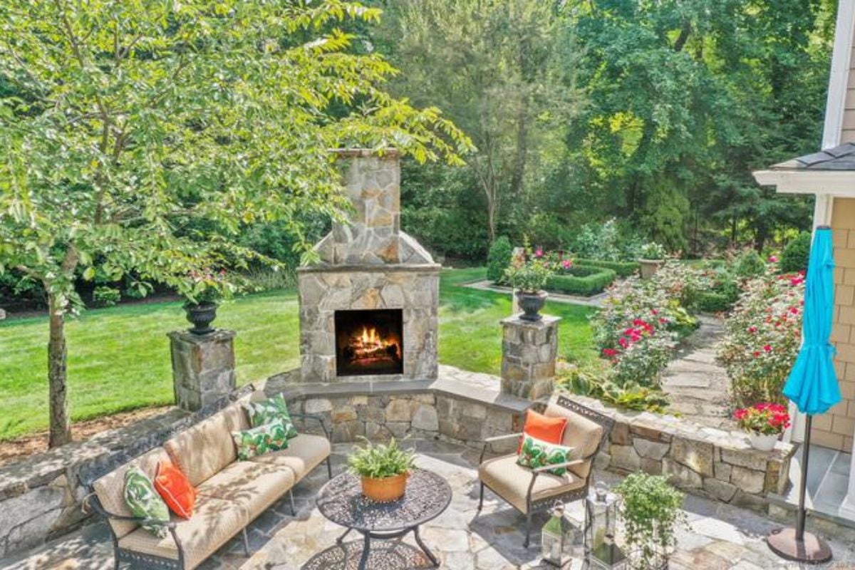 A patio with a fireplace, couch, chair, coffee table, and plants.