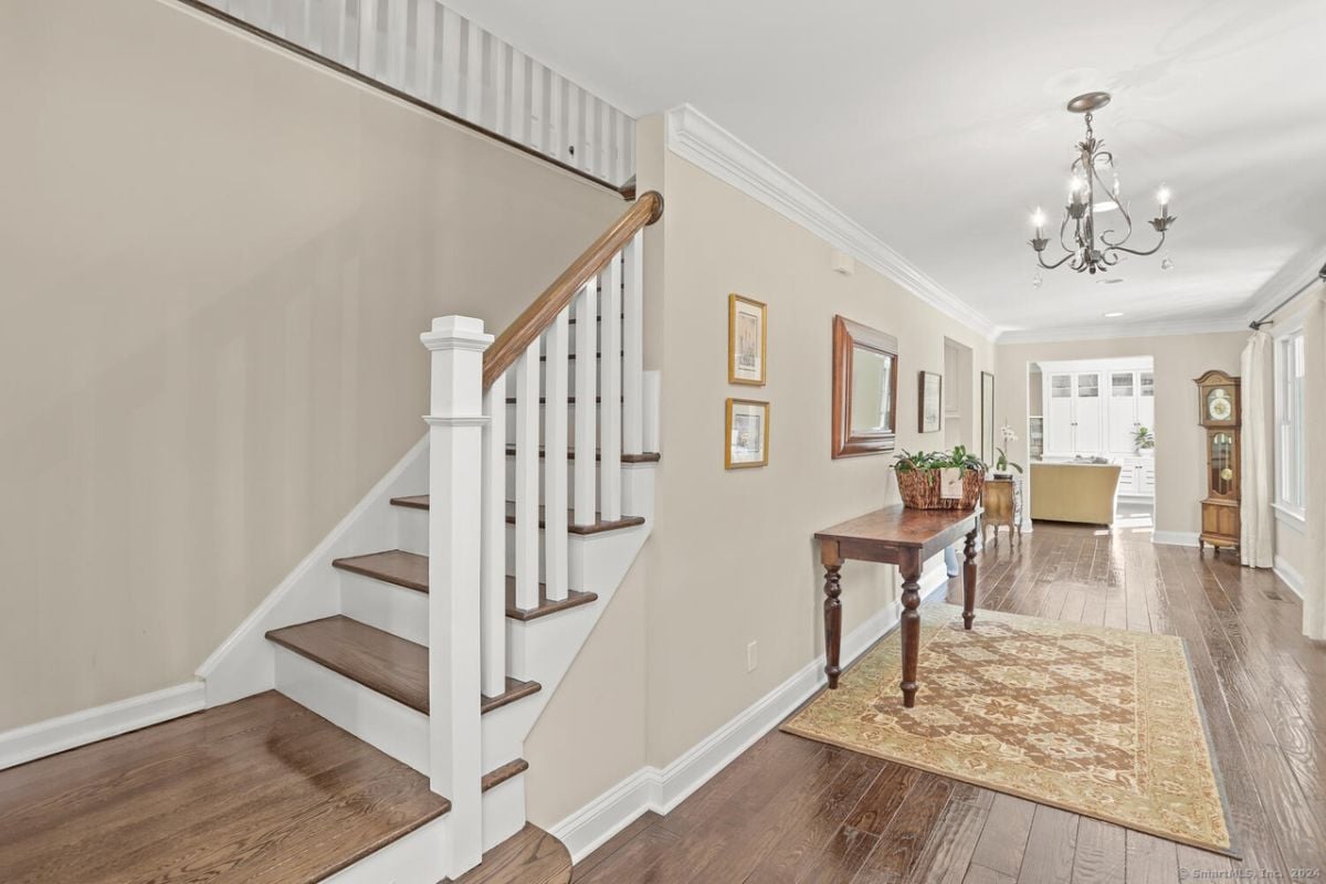 A foyer with wooden floors, a rug, a table, and a chandelier.