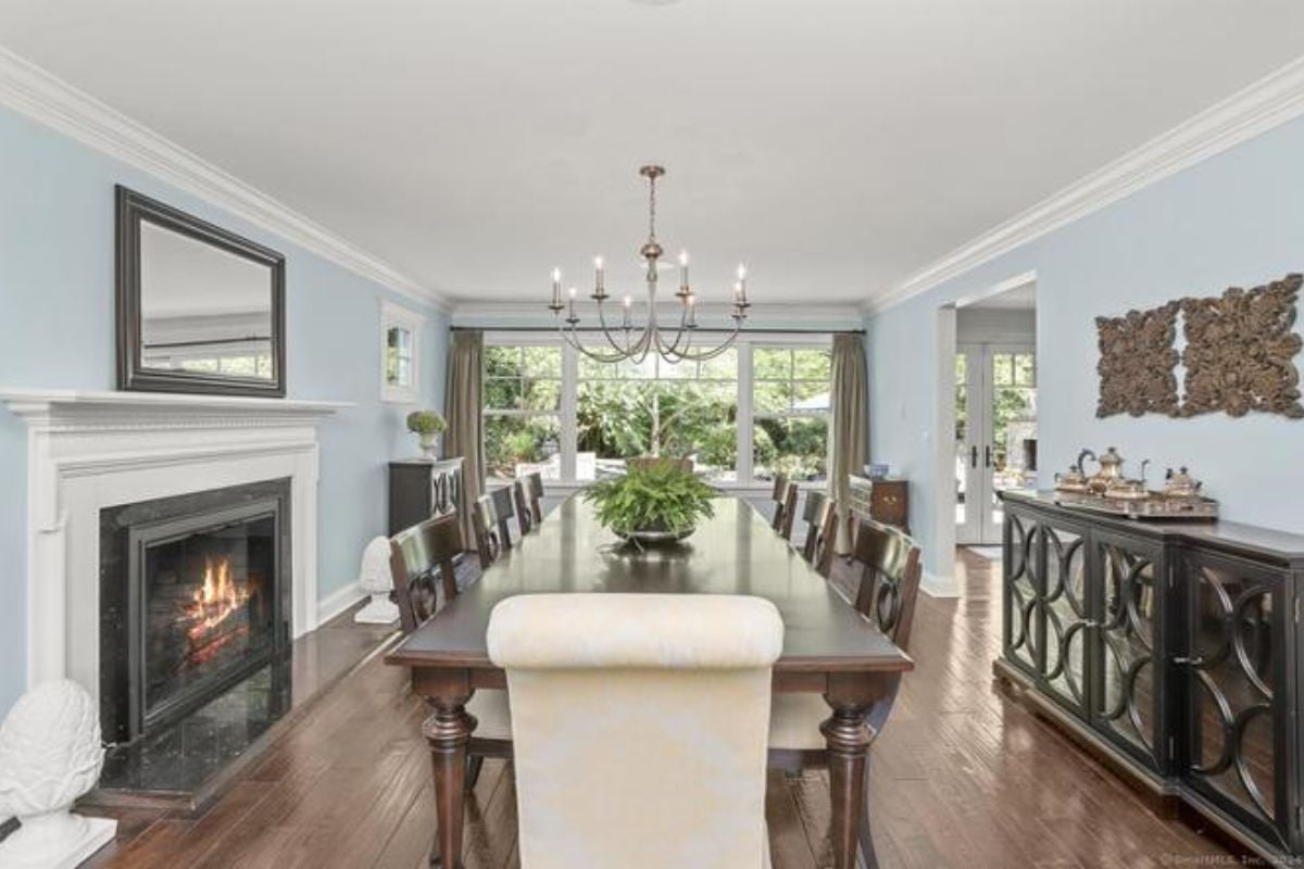 A dining room with a fireplace, mirror, chandelier, and a dining table surrounded by chairs.