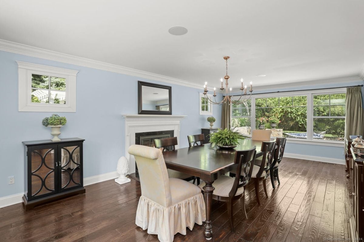 A dining room with a fireplace, mirror, chandelier, and a dining table surrounded by chairs.