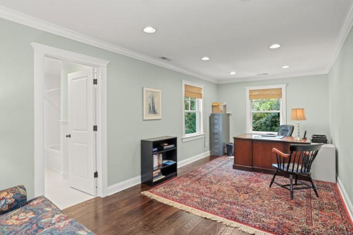 A home office with a rug, cabinet, windows, desk, and chairs.