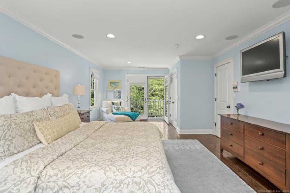 A bedroom with a bed, TV, rug, studio couch, cabinet and blue walls.