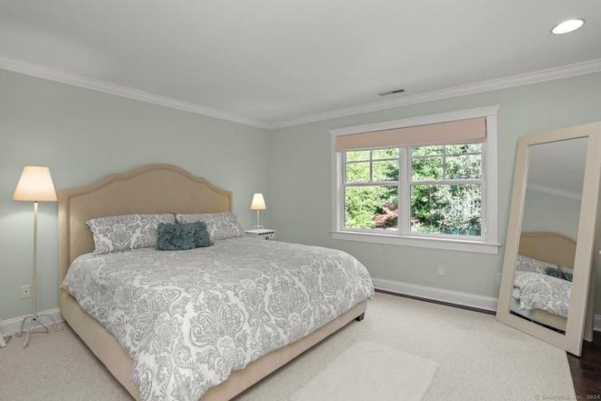 A bedroom with a bed, blue walls, a window, and a mirror.
