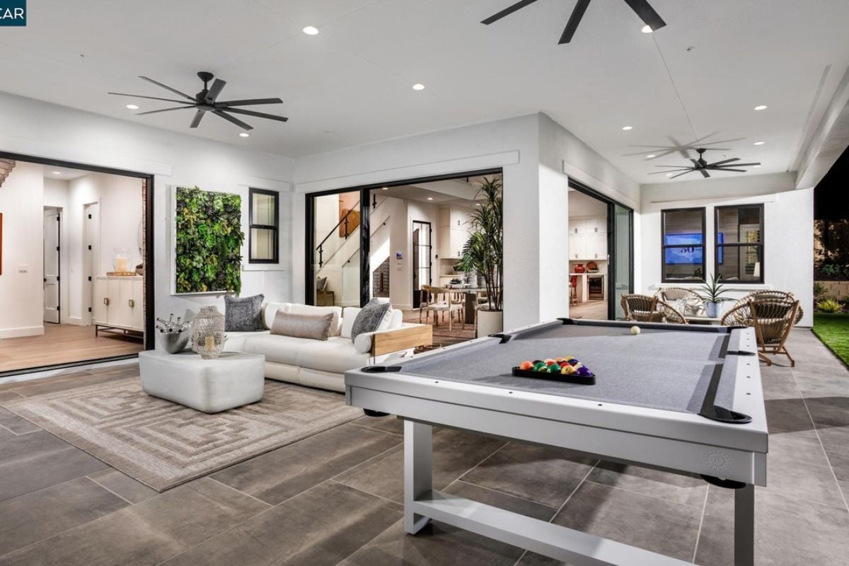 An outdoor living space with ceiling fans, a couch, and a pool table.