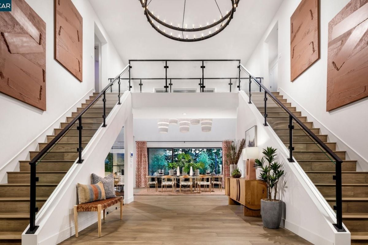 A foyer with a cabinet, potted plants, a bench, and a grand staircase.