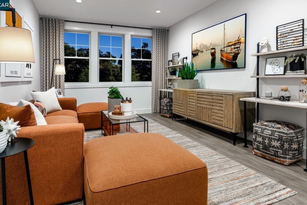 A living room with a cabinet, shelf, TV, windows, couches, and a glass center table.