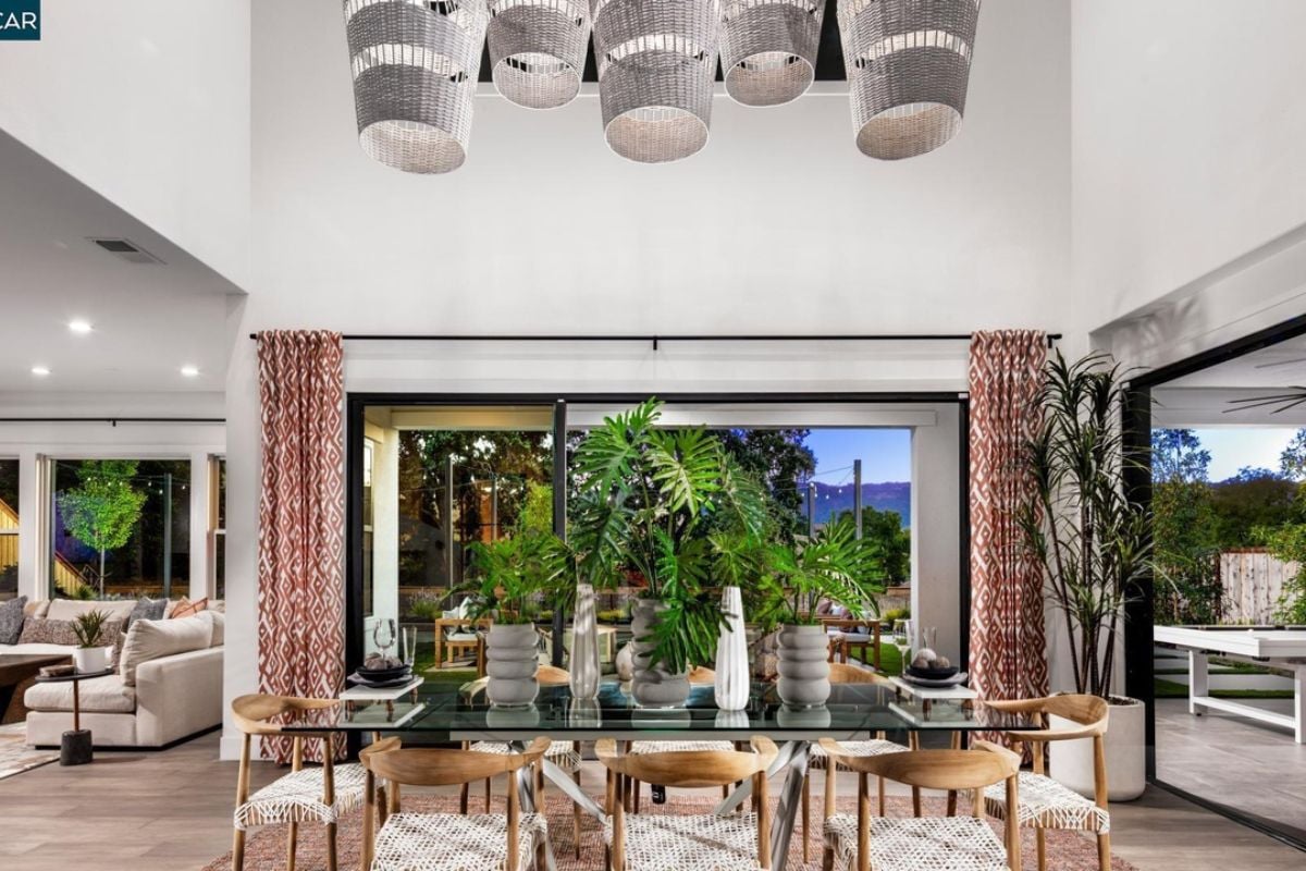 A dining room with windows and a glass dining table surrounded by chairs.