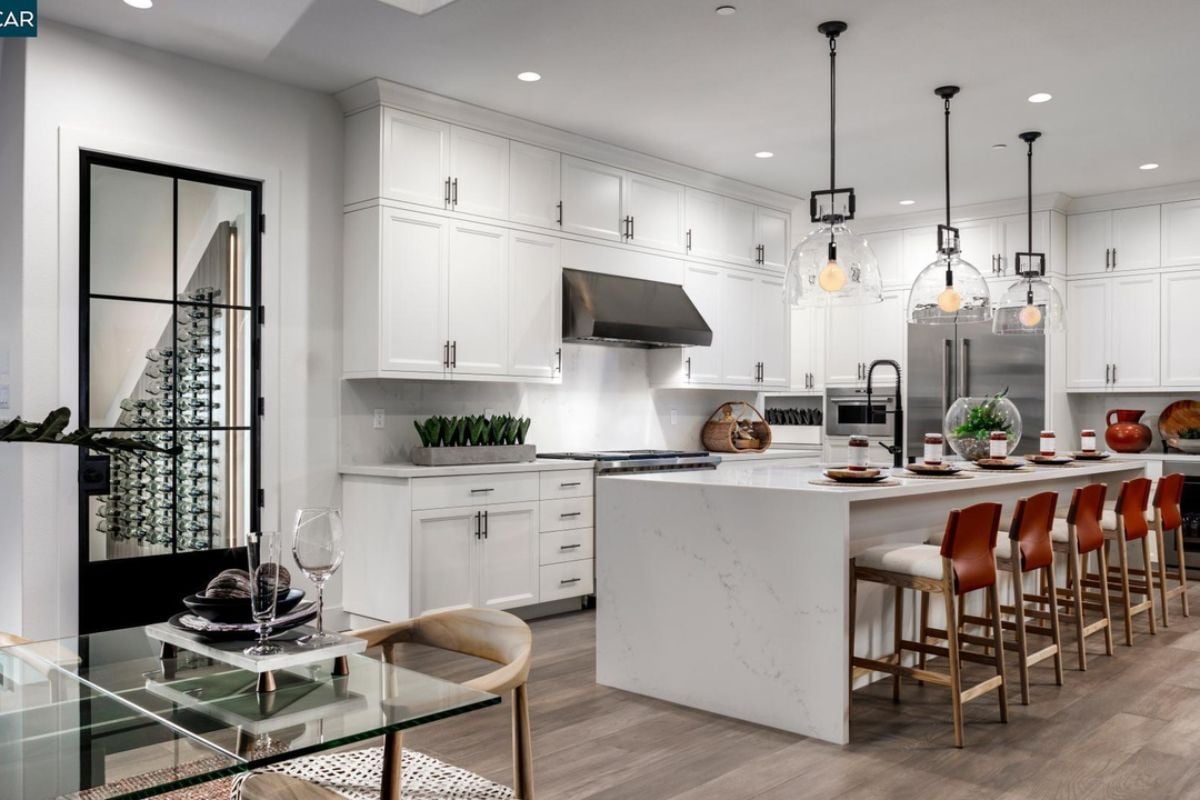 A kitchen with an island, chairs, countertops, cabinets, and kitchen appliances.