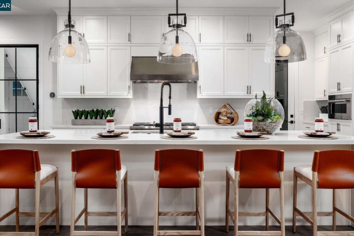 A kitchen with an island, chairs, sink, countertop, cabinets, and kitchen appliances.