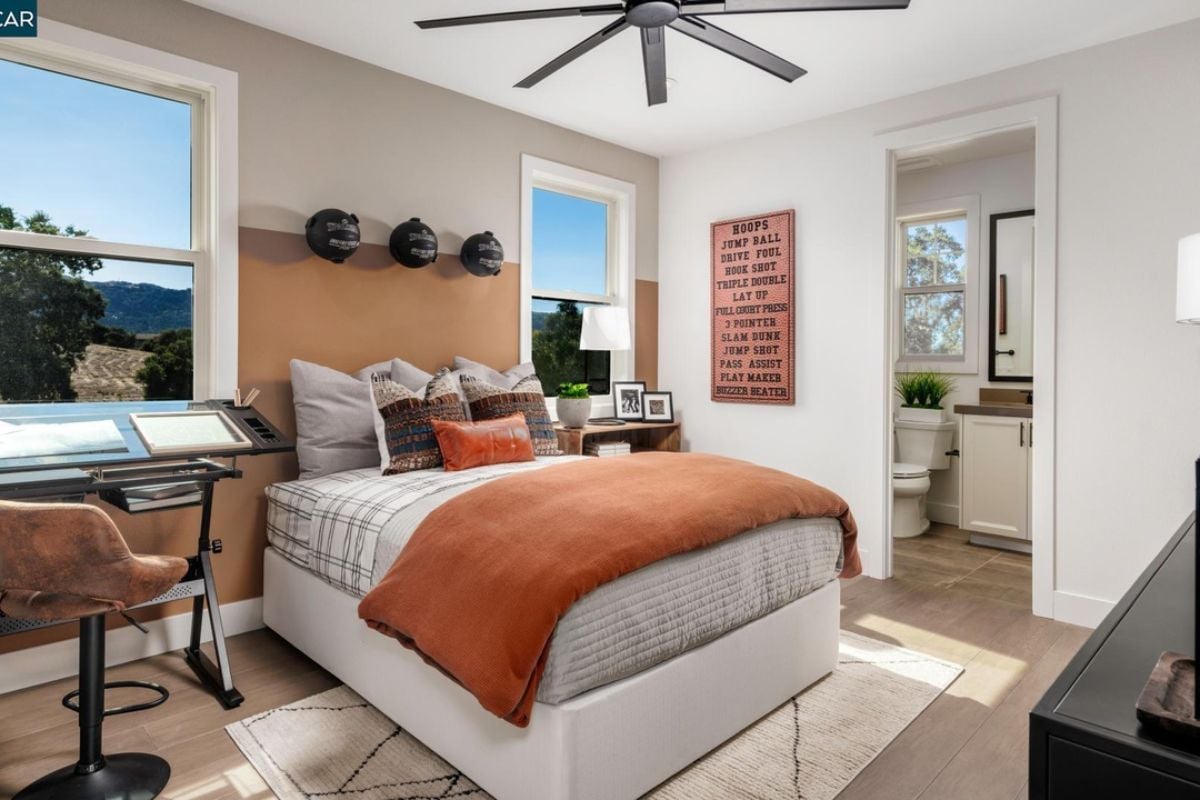A bedroom with a bed, ceiling fan, windows, nightstand, and chair.
