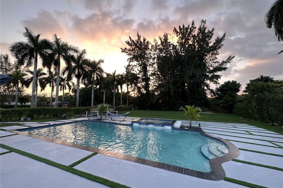 A swimming pool with a Jacuzzi surrounded by plants and trees.