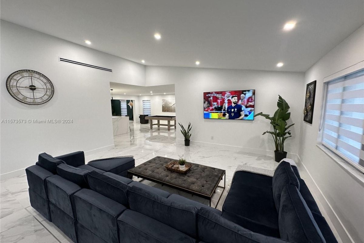 A living room with a tiled floor, TV, potted plants, couch, and a center table.